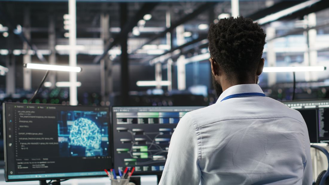 Profissional analisando sistemas digitais em monitores, representando como aplicar inteligência artificial em processos e dados empresariais.